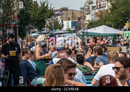 Clapham wartet auf Tische mit einer Gesichtsmask an der Northcote Road und ist nun für Autos gesperrt und öffnet an einem heißen Sommertag die Straße für Restaurants und Bars. Stockfoto