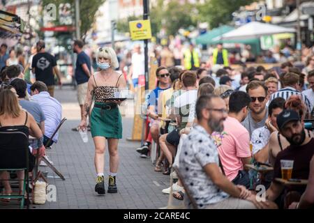 Clapham wartet auf Tische mit einer Gesichtsmask an der Northcote Road und ist nun für Autos gesperrt und öffnet an einem heißen Sommertag die Straße für Restaurants und Bars. Stockfoto