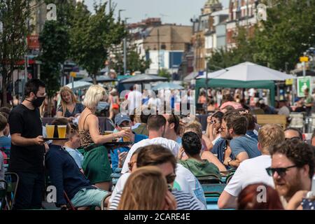 Clapham wartet auf Tische mit einer Gesichtsmask an der Northcote Road und ist nun für Autos gesperrt und öffnet an einem heißen Sommertag die Straße für Restaurants und Bars. Stockfoto