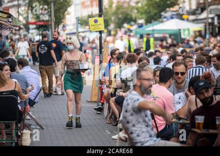 Clapham wartet auf Tische mit einer Gesichtsmask an der Northcote Road und ist nun für Autos gesperrt und öffnet an einem heißen Sommertag die Straße für Restaurants und Bars. Stockfoto