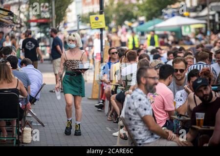 Clapham wartet auf Tische mit einer Gesichtsmask an der Northcote Road und ist nun für Autos gesperrt und öffnet an einem heißen Sommertag die Straße für Restaurants und Bars. Stockfoto