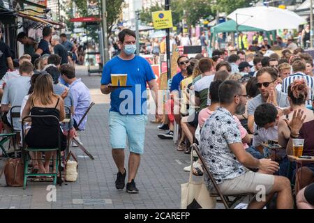 Clapham wartet auf Tische mit einer Gesichtsmask an der Northcote Road und ist nun für Autos gesperrt und öffnet an einem heißen Sommertag die Straße für Restaurants und Bars. Stockfoto