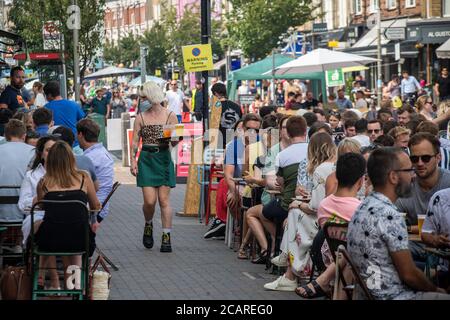 Clapham wartet auf Tische mit einer Gesichtsmask an der Northcote Road und ist nun für Autos gesperrt und öffnet an einem heißen Sommertag die Straße für Restaurants und Bars. Stockfoto