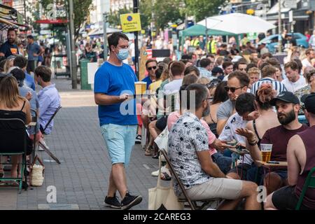 Clapham wartet auf Tische mit einer Gesichtsmask an der Northcote Road und ist nun für Autos gesperrt und öffnet an einem heißen Sommertag die Straße für Restaurants und Bars. Stockfoto