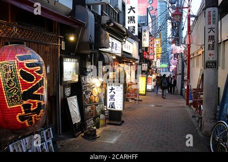 Tokio, Japan - 13. März 2018: Beleuchtete Gasse mit Bars und Izakaya (Pub für After-Work-Trinken) am Abend mit wenigen Menschen zu Fuß vorbei. Stockfoto