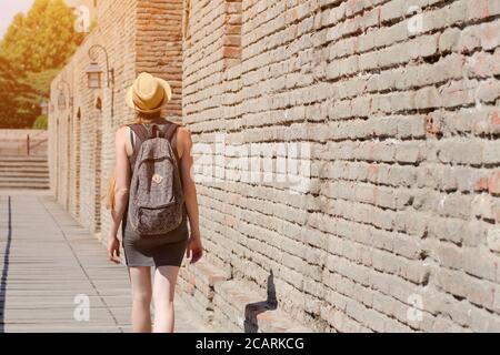 Mädchen in einem Hut und mit einem Rucksack zu Fuß entlang der Stadtmauer. Sonniger Tag Stockfoto