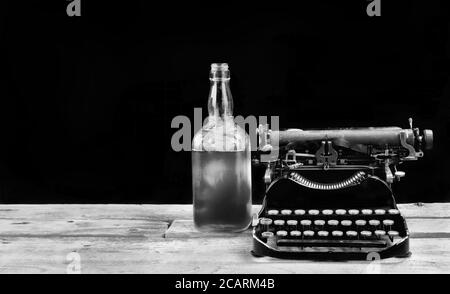 Antike tragbare Schreibmaschine aus dem Jahr 1917 mit Whisky-Flasche mit Platz für Ihren Typ in schwarz und weiß. Stockfoto