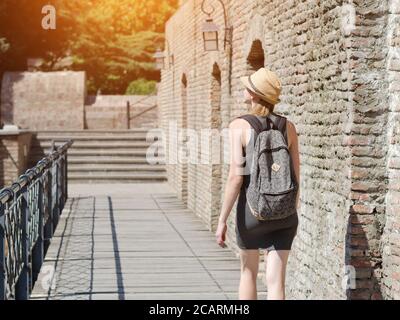 Mädchen in einem Hut und mit einem Rucksack zu Fuß entlang der Stadtmauer. Sonniger Tag Stockfoto