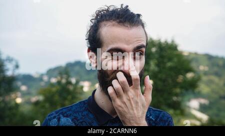 Junger hübscher Hipster-Mann berührt Gesicht und lächelt Stockfoto