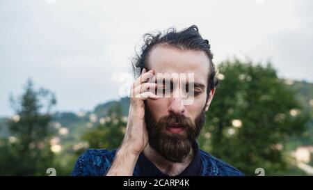 Junger hübscher Hipster-Mann mit langen Haaren und Bart leiden Ein Kopfschmerz sieht traurig aus Stockfoto