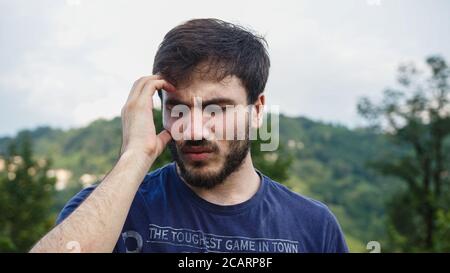 Der junge Mann im T-Shirt ist gestresst und hat Kopfschmerzen In einer natürlichen Umgebung Stockfoto