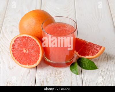Glas frisch gepresster Grapefruitsaft mit Fruchtfleisch und ganzen, halb und Viertel Grapefruits auf einem weißen Holztisch. Vegetarische, Rohkost Ernährung. Stockfoto
