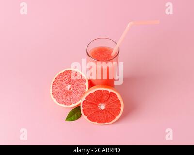 Glas frisch gepresster Grapefruitsaft mit Fruchtfleisch, Trinkhalm und zwei Hälften Grapefruit auf rosa Hintergrund. Vegetarische, Rohkost Ernährung. Stockfoto