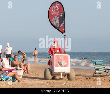 Punta Umbria, Huelva, Spanien - 7. August 2020: Eine weibliche Straßenverkäuferin, die Eis am Strand verkauft. Der Verkäufer trägt eine schützende oder medizinische Gesichtsmaske Stockfoto