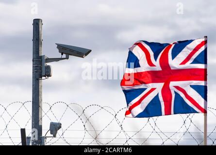 Flagge des Vereinigten Königreichs mit Überwachungskamera und Stacheldraht, Konzeptbild Stockfoto