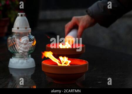 Traditionelle brennende Grabkerzen auf einem Grab während aller Seelen Tag im Hintergrund alte Frau Hand Feuer Kerze Stockfoto