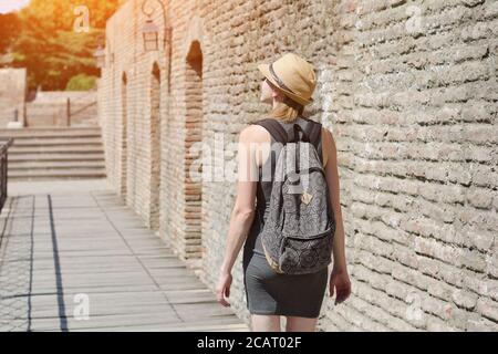 Mädchen in einem Hut und mit einem Rucksack zu Fuß entlang der Stadtmauer. Sonniger Tag Stockfoto