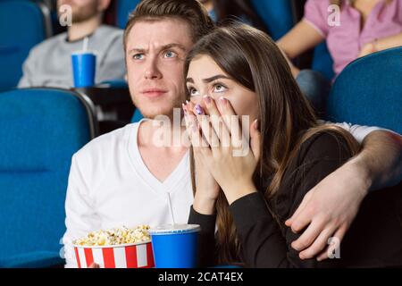 Was zum Teufel? Porträt eines gestörten jungen, gutaussehenden Mannes, der seine verängstigte Freundin umarmt, während er Filme im Kino ansieht Stockfoto