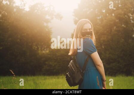 Schöne blonde Frau mit Maske im Sonnenuntergang im Freien in blau Kleid Stockfoto