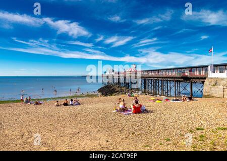 Menschen, die am Strand am Herne Bay Pier in Herne Bay, Kent, Großbritannien, sitzen Stockfoto