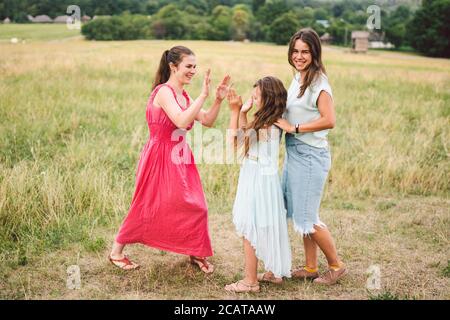 Drei Erwachsene kaukasische Schwestern spielen und haben Spaß auf dem Feld. Eine Familie von drei jungen Frauen lacht und verbringt die Sommerzeit in der Natur. Glücklich Stockfoto