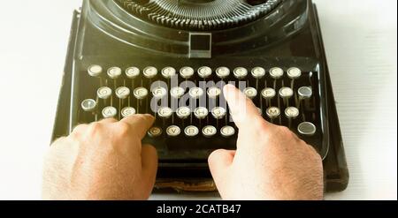 Männliche Hände, die einen Text schreiben, indem sie die Tasten einer alten Schreibmaschine eingeben. Vintage-Artikel und alte mechanische Technik Stockfoto