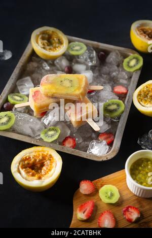 Hausgemachtes tropisches Eis oder Eiszapfen garniert mit Eisstücken und Kiwi, Passionsfrucht und Erdbeerscheiben, Draufsicht Stockfoto