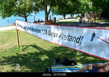 Sipplingen Am Bodensee, Deutschland. August 2020. Sonnenanbeter liegen auf ihren Badetüchern an der Uferpromenade am Bodensee, während im Vordergrund ein Schild steht: 'Bitte halten Sie einen Abstand von mindestens 1.5 Metern'. Die Behörden appellieren an Touristen, die Regeln der Entfernung zu beachten. Quelle: Felix Kästle/dpa/Alamy Live News Stockfoto