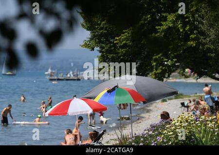 Sipplingen Am Bodensee, Deutschland. August 2020. Sonnenanbeter liegen an der Uferpromenade am Bodensee unter ihren Sonnenschirmen. Die Behörden appellieren an Touristen, sich an die Regeln der Entfernung zu halten. Quelle: Felix Kästle/dpa/Alamy Live News Stockfoto
