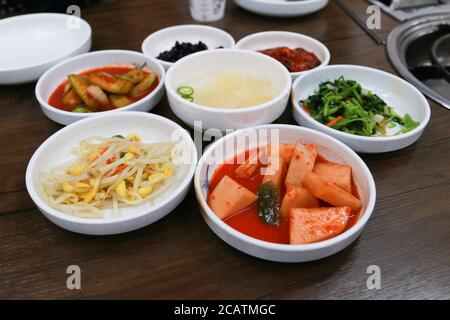 Koreanische traditionelle Beilage Rettich, Kimchi, Bohnensprossen, Gemüse, Algen, Gurken und Suppe auf einem Holztisch. Stockfoto