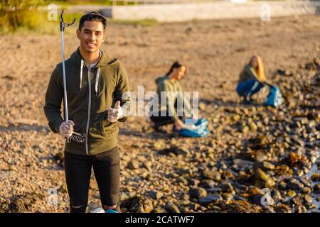 Mann zeigt Daumen nach oben mit Umwelt Schutz Freiwilligen am Strand Stockfoto