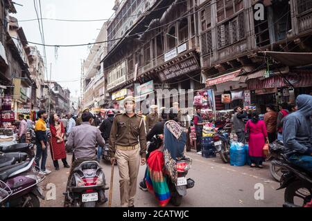 Agra / Indien - 22. Februar 2020: Umweltportrait eines jungen Militärs, der mit einem Stock durch eine geschäftige Straße in der Innenstadt von Agra geht Stockfoto