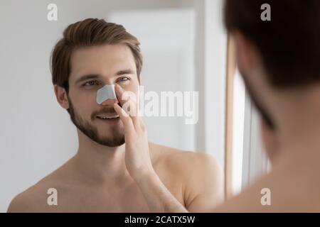 Spiegelreflexion lächelnder Mann, der Anti-Schwarzkopfmaske auf der Nase aufwendet Stockfoto