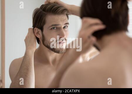Nahaufnahme ängstlicher junger Mann, der die Haare berührt und in den Spiegel schaut Stockfoto