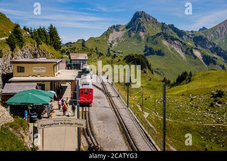 Schynige Platte, Berner Oberland, Schweiz - 1. August 2019 : Hochwinkelansicht am Bahnhof, Touristen und roter Zug in schöner Bergpanora Stockfoto