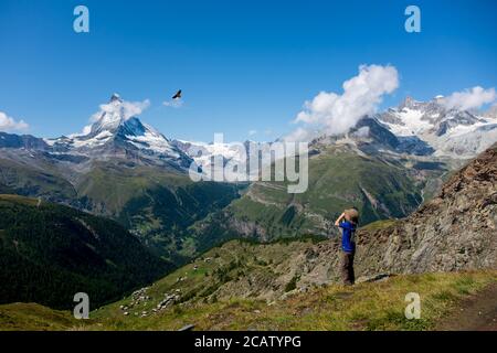 Kleiner Junge beobachtet einen Greifvogel durch ein Fernglas mit Schweizer Bergen als Hintergrund. Stockfoto
