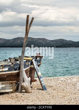 Leeres altes rostiges Fischerboot am Ufer des Meeres an einem ruhigen bewölkten Tag. Hügel im Hintergrund. Vertikale Aufnahme. Stockfoto