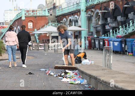Brighton, Großbritannien. August 2020. Ein lokaler Händler fegt einen Teil des Mülls von der Vorderseite seines Geschäfts am Brighton Beach. Kredit: James Boardman/Alamy Live Nachrichten Stockfoto