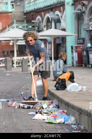 Brighton, Großbritannien. August 2020. Ein lokaler Händler fegt einen Teil des Mülls von der Vorderseite seines Geschäfts am Brighton Beach. Kredit: James Boardman/Alamy Live Nachrichten Stockfoto
