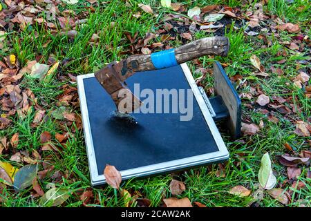 AX zum Zertrümmern eines Computerbildschirms auf dem Grashintergrund Stockfoto