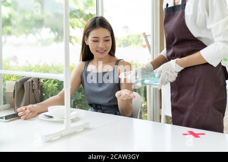 Kellnerin drücken Alkohol Gel Hand Desinfektionsmittel für Kunden am Esstisch für die Hygiene Handreinigung reduzieren Infektion und Verbreitung Coronavirus covid-19 pa Stockfoto