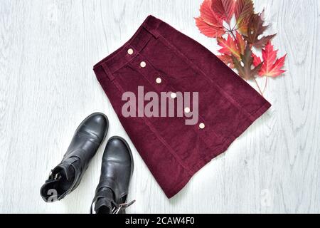 Burgunder Wildlederrock, schwarze Stiefel und rote Blätter. Modisches Konzept. Stockfoto