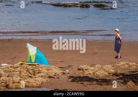 Eine Frau mit blauem Kleid und weißem Hut Blickt in die Ferne, während er in der Nähe eines Windschutzschalters steht Stockfoto