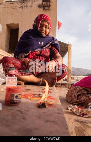 Pushkar / Indien - 10. März 2020: Indische Frauen aus Rajasthan tragen rote traditionelle Kleidung sitzt in der Treppe in der Nähe von Pushkar heiligen See machen Angebot mit Kerze Stockfoto