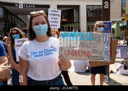 Oxford, Großbritannien. August 2020. NHS-Arbeiter und -Unterstützer nahmen an einer Kundgebung auf dem Bonner Platz in Oxford Teil, in der sie für Lohngerechtigkeit für alle NHS-Arbeiter aufriefen und protestierten, eine Lohnerhöhung zu fordern, um ihre Bemühungen während der covid Pandemie widerzuspiegeln.Dies war eine von etwa 38 ähnlichen Kundgebungen in ganz Großbritannien. Die Protestierenden behielten soziale Distanzierung aufrecht und trugen Masken. Während sie den Rednern zuhörten, hielten viele Plakate, die ihre Beschwerden und wie sie sich unterschätzt fühlten, hervorhoben. Im Bild, NHS Arbeiter mit Plakat - Krankenschwestern überarbeitet und unterbezahlt. Quelle: Stephen Bell/Alamy Stockfoto