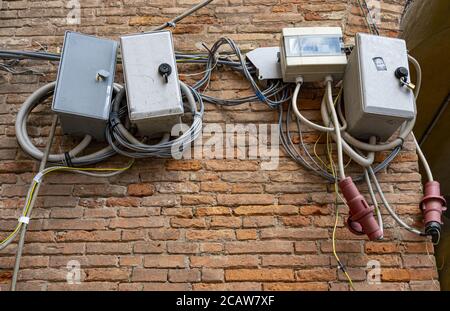 Ferrara, Italien. 6. August 2020. Chaotische Verbindungen und Verteilerkästen von elektrischen Kabeln an einer Ziegelwand Stockfoto