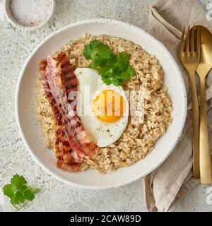 Haferflocken, Spiegelei, gebratener Speck. Herzhaftes, fettes, kalorienreiches Frühstück, Blick von oben Stockfoto