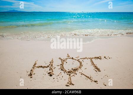 HOT Wort und Sonne Symbol auf den Sand geschrieben Tropischer Meeresstrand Stockfoto