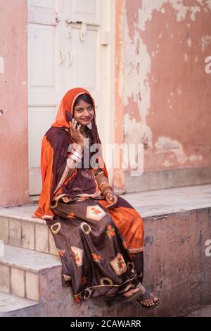 Jodhpur / Indien - 18. März 2020: Porträt der schönen jungen Rajasthani Frau mit Juwelen auf ihrem Gesicht und traditionelle Kleidung sitzen mit Telefon Stockfoto