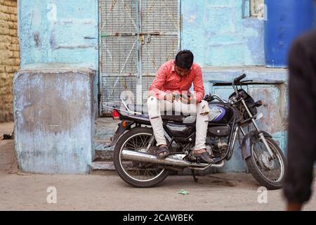 Jodhpur / Indien - 18. März 2020: Junger Inder sitzt auf dem Motorrad mit dem Telefon Stockfoto